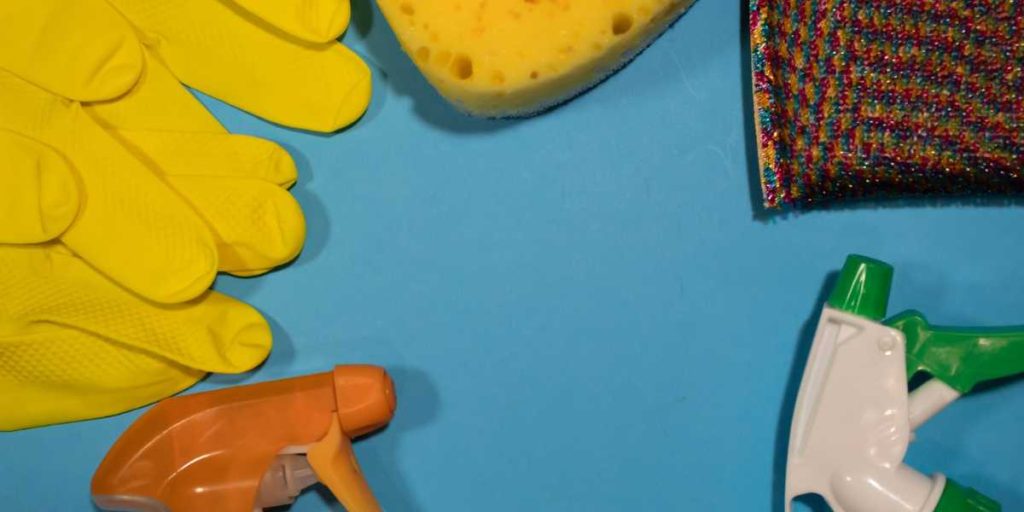 Rubber gloves, cleaning sponges, and spray bottles for house cleaning on a light blue background